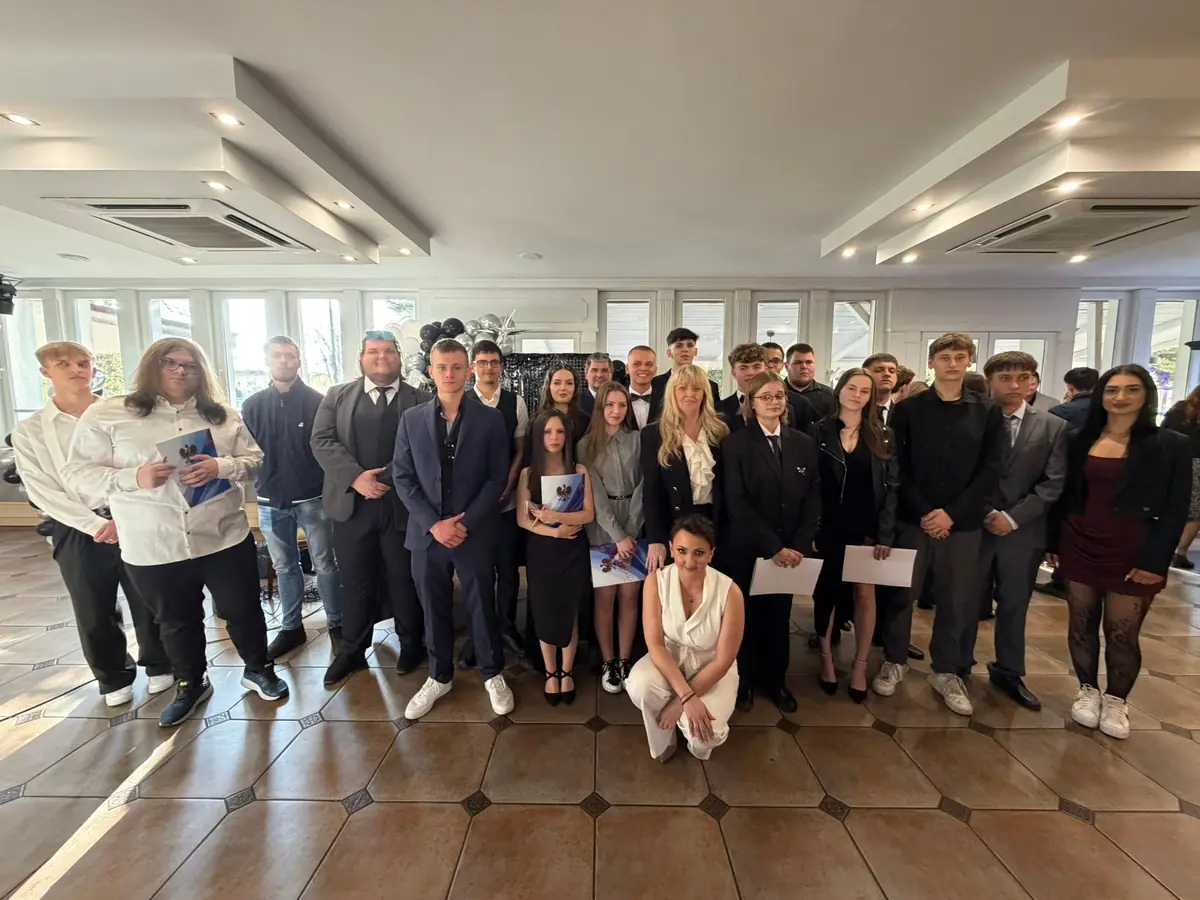 Grupowe zdjęcie absolwentów w strojach galowych ze świadectwami w sali